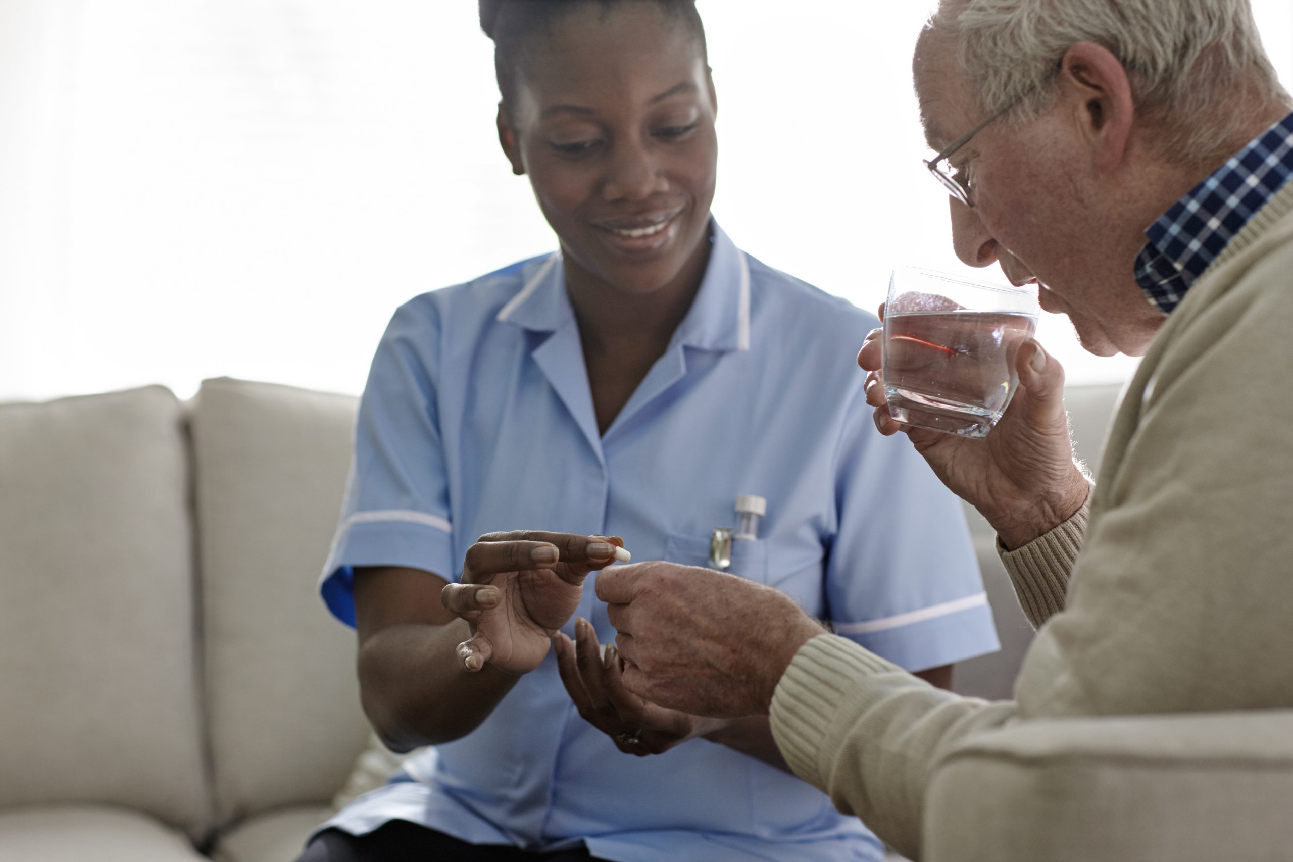 Female Doctor giving medication to elderly patient sitting on sofa
